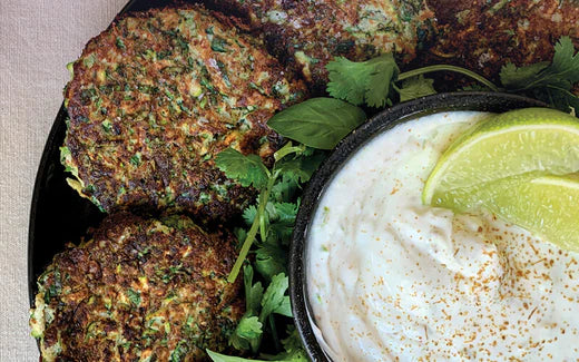black plate with zucchini fritters, two limes, and cumin lime yogurt with garnish of cilantro refreshing snack appetizer