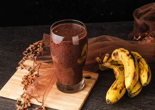 A refreshing glass of cocoa banana smoothie filled with bananas and a variety of colorful fruits, showcasing a healthy beverage option.