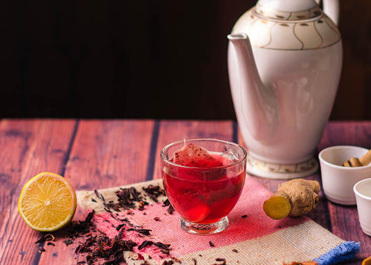 A tea pot and hibiscus tea with various ingredients arranged on a wooden table, creating a cozy tea preparation scene.