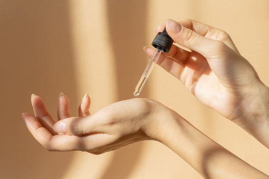 A person grasping a bottle of oil, showcasing the product in their hand with a neutral background.