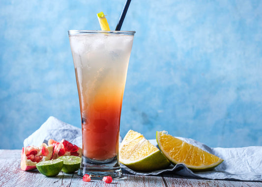 A vibrant pomegranate highball cocktail featuring orange and lime garnished, elegantly placed on a rustic wooden table.