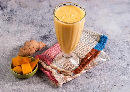 A glass of fresh turmeric mango lassi juice beside a bowl filled with mango slices and ginger