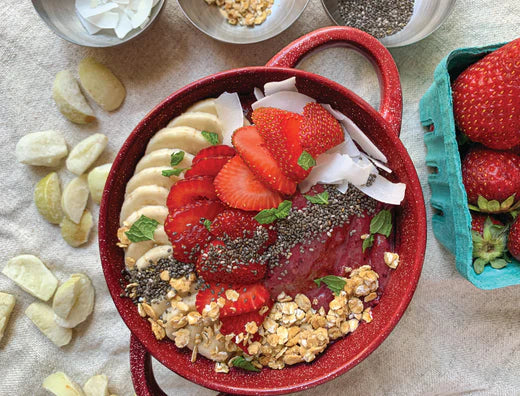 A vibrant acai bowl filled with assorted fresh fruits, including apples, bananas, and oranges, arranged beautifully.