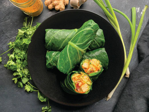 A plate filled with fresh green leafy chicken curry wraps alongside a bottle of ginger, showcasing a healthy meal option.