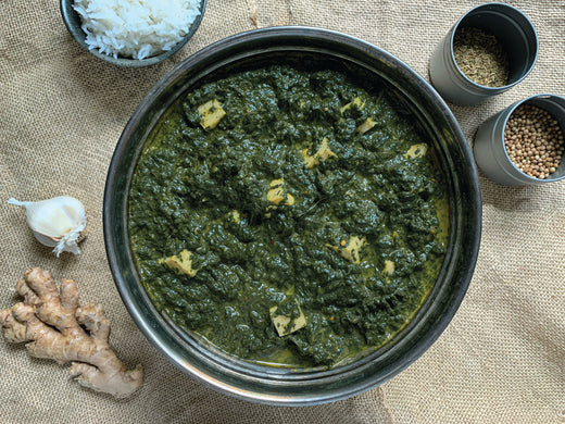 A bowl filled with vibrant green food, garnished with spices and various ingredients, showcasing a colorful culinary creation.