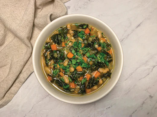 A hearty bowl of white bean kale soup featuring an assortment of greens and beans, emphasizing a healthy dish.