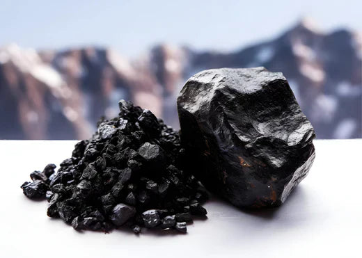 A pile of shilajit and a rock positioned in front of a majestic mountain landscape, showcasing natural resources and terrain.