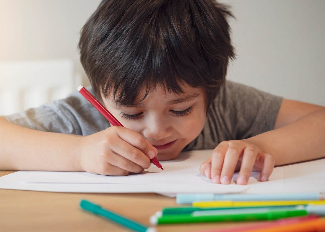 A young boy focused on drawing on paper with a pencil, showcasing his creativity and concentration.