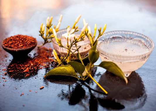 A glass filled with liquid beside a bowl of assorted spices on a neutral background.