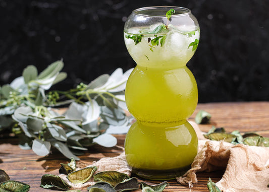 A glass of vibrant green meta matcha drink sits on a table, accompanied by fresh leaves, creating a refreshing ambiance.