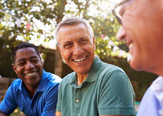 Three men joyfully laughing together under the warm sun, showcasing camaraderie and happiness in a bright outdoor setting.