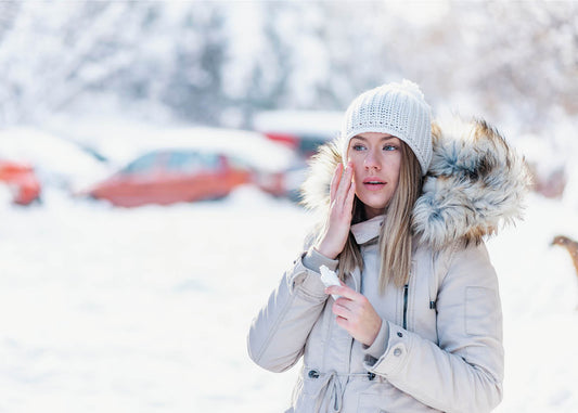 A woman wearing a winter coat holds her hand to her face, reflecting a thoughtful expression amidst a chilly atmosphere.