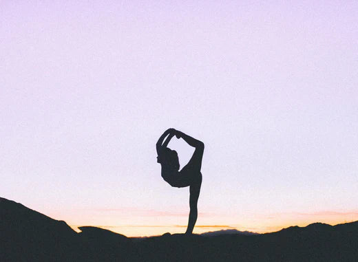 A person practicing yoga in the serene desert during a vibrant sunset, surrounded by golden sands and a colorful sky.