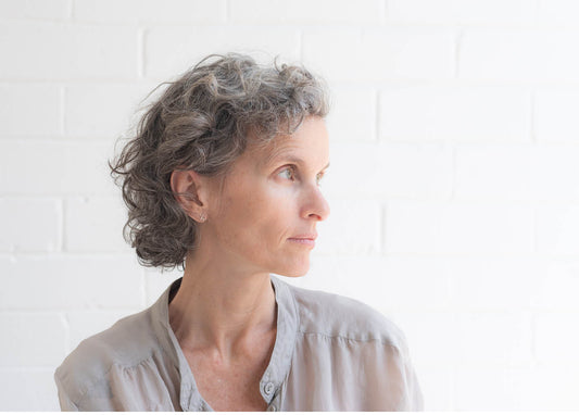 A woman with short hair wearing a gray shirt, standing confidently with a neutral expression.