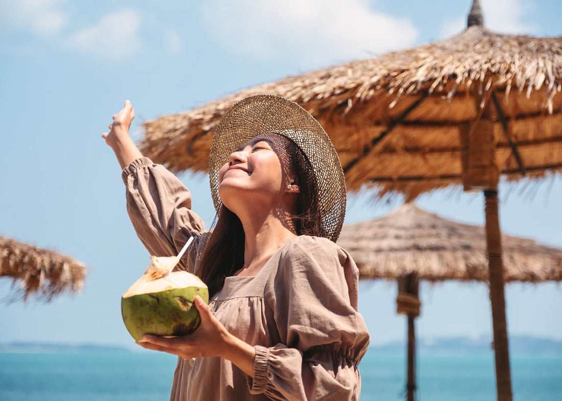 woman at a beach holding a coconut drink.
